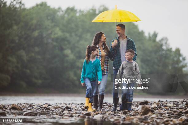 glückliche familie im gespräch beim spazierengehen auf einem regen am flussufer. - mother protecting from rain stock-fotos und bilder