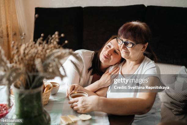 volunteer hugs an elderly woman over a cup of tea, enjoying the company - assisted living community stock pictures, royalty-free photos & images