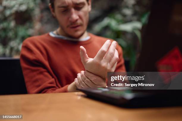 man massaging painful wirst while working at laptop. - hold wrists fotografías e imágenes de stock