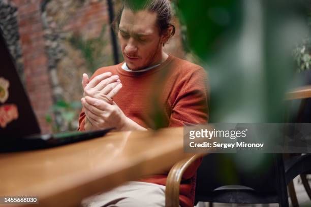 man massaging painful wirst while working at laptop. - rheumatism stock pictures, royalty-free photos & images