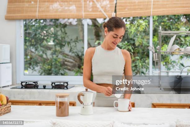 lächelnde frau, die proteinpulver in einen kaffee gibt - protein powder stock-fotos und bilder