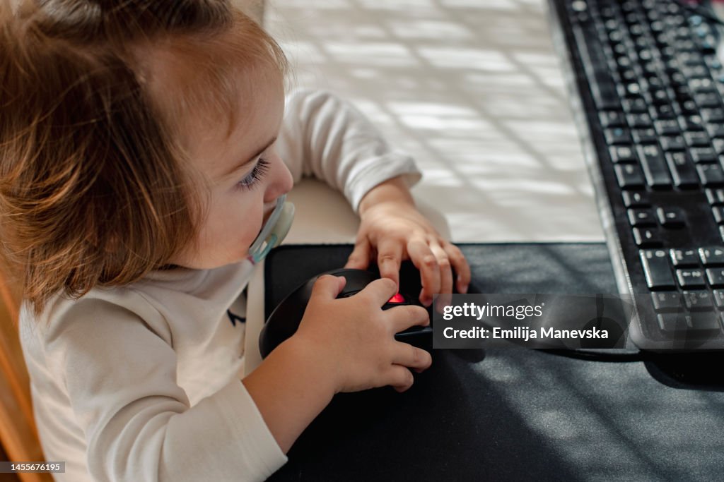 Baby girl sitting at a desk playing with a computer keyboard