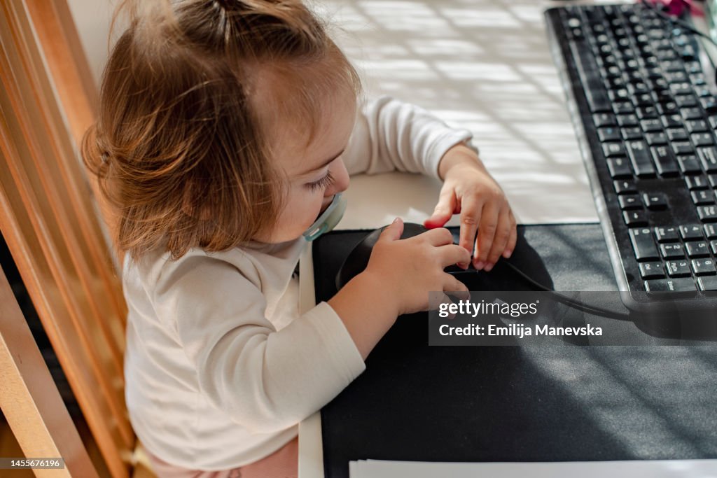 Baby girl sitting at a desk playing with a computer keyboard