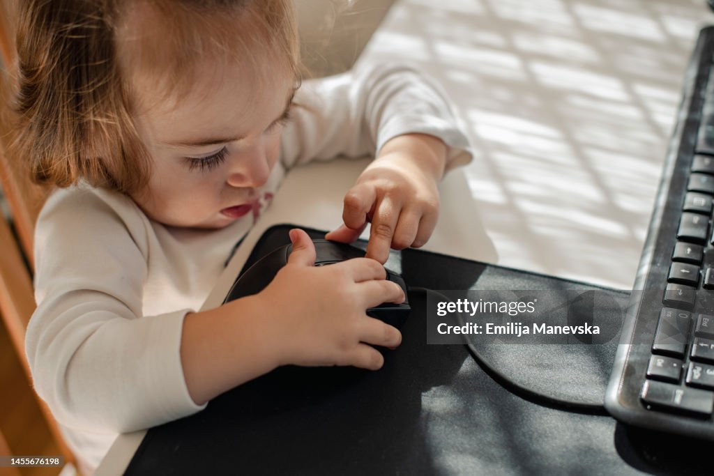 Baby girl sitting at a desk playing with a computer keyboard