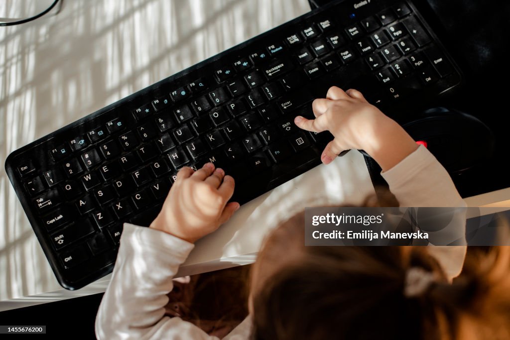 Baby girl sitting at a desk playing with a computer keyboard