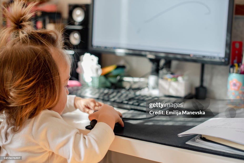 Baby girl sitting at a desk playing with a computer keyboard