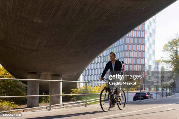 businessman riding bicycle under bridge while commuting to work - commuter man europe bike stock pictures, royalty-free photos & images