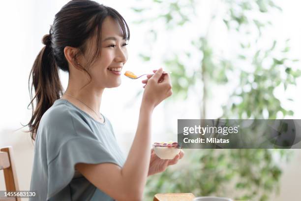 woman eating breakfast in the living room - 30s woman eating stock pictures, royalty-free photos & images