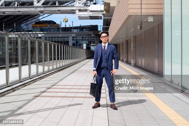 a young businessman in the city, on the move, a man in a suit with a laptop bag, standing legs apart on a walkway - businessman in suit ストックフォトと画像
