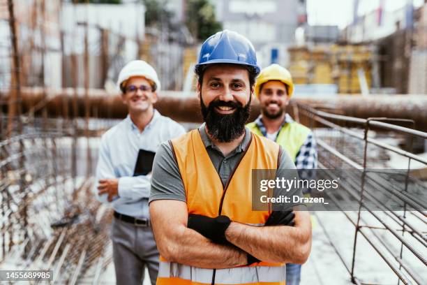 engineers on construction site, looking at camera and smiling. employment in housing and real estate sector - construction worker pose stock pictures, royalty-free photos & images