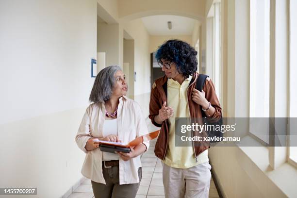 student and professor walking and talking on campus - academia stockfoto's en -beelden