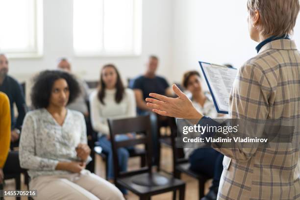 middle aged woman giving a talk at a meeting - community college stockfoto's en -beelden