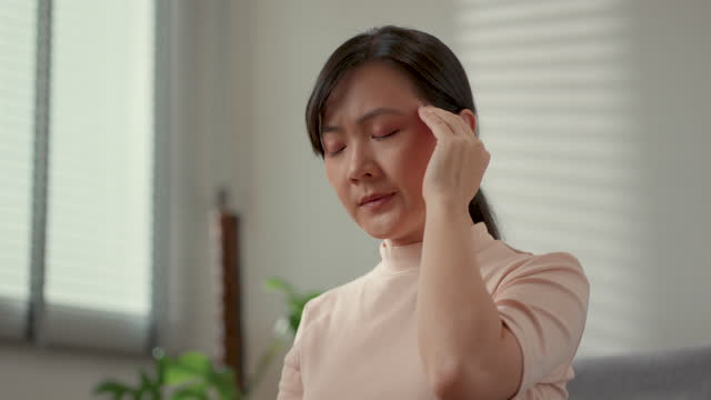 Asian woman was sick with headache sitting on sofa in living room at home.