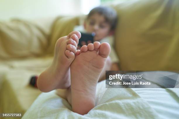 relaxed boy using cell phone on couch at home - toe stock pictures, royalty-free photos & images