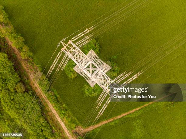 aerial view/a high-voltage electric pole located in the middle of a field. - corriente-de-alto-voltaje fotografías e imágenes de stock