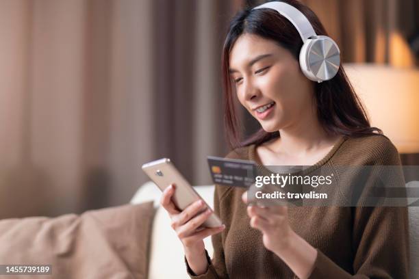 close-up cheerful happiness asian young adult female woman in casual cloth use smartphone online shopping with credit card enjoy purchase discount cloth on sofa in living room at home - debt free stock pictures, royalty-free photos & images