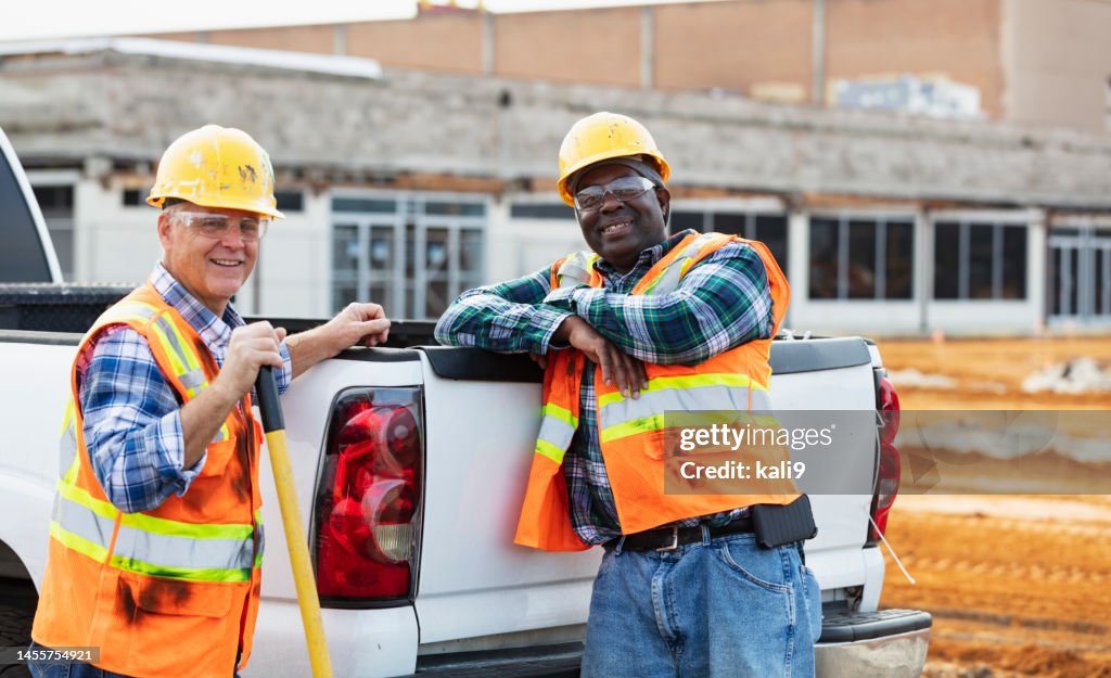 Two construction workers standing behind pickup truck