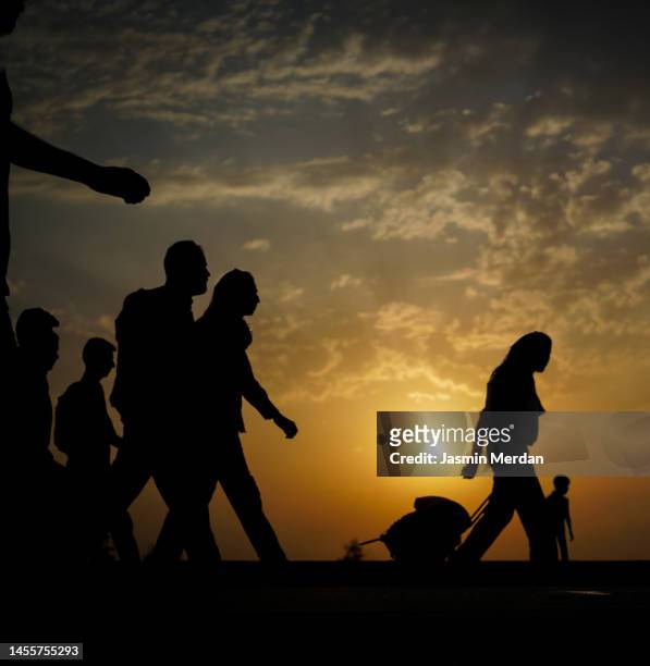 silhouette of people crossing land on sunset - displaced people ストックフォトと画像