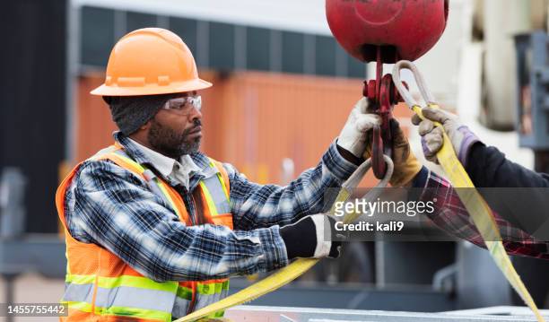 african-american man prepares object to lift with crane - strap stock pictures, royalty-free photos & images