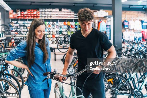 mann zeigt kundin neues rennrad im bikeshop - sportgeschäft stock-fotos und bilder