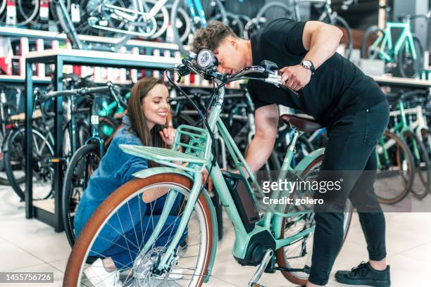 man showing female customer new e- bike in bikeshop - bike shop stockfoto's en -beelden