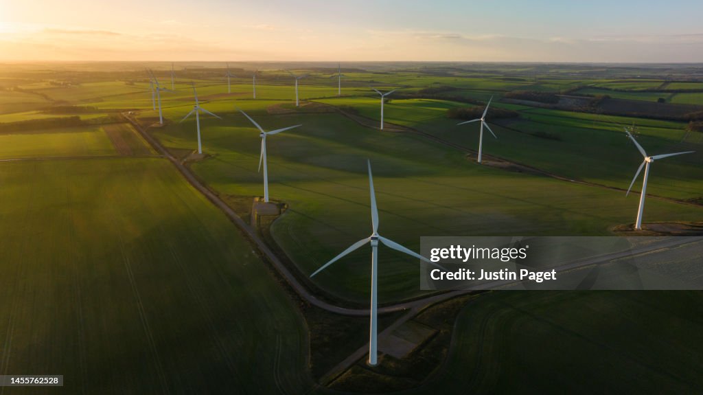 Aerial/Drone view of a wind farm with multiple wind turbines at sunrise