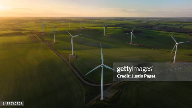 aerial/drone view of a wind farm with multiple wind turbines at sunrise - umweltthemen stock-fotos und bilder