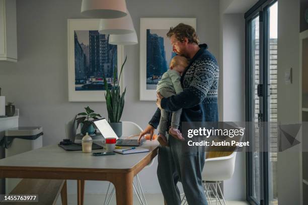 a mature man checks his emails on his laptop whilst he holds his sleeping baby girl - house husband stock pictures, royalty-free photos & images