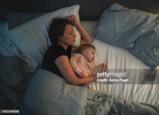 a mature mother asleep with her baby girl. the warm light from the sidelight washes over them - baby sleep stock-fotos und bilder