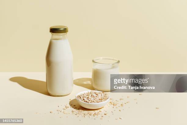 oat milk in glass bottle and glass, oatmeal in a white bowl on beige background. healthy vegan non-dairy organic drink with flakes. lactose-free milks in minimal flat lay style. top view, copy space. - dairy product fotografías e imágenes de stock
