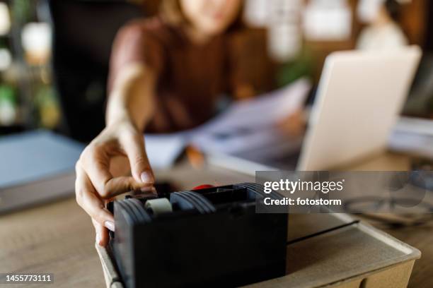mujer joven buscando cinta adhesiva en su escritorio mientras hace un proyecto - tape dispenser fotografías e imágenes de stock