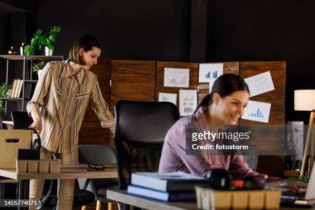 young businesswoman working at her desk while her colleague is packing after getting fired - day 1 stock pictures, royalty-free photos & images