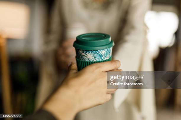 young woman handing her female colleague a cup with coffee during office break - reusable coffee cup stock pictures, royalty-free photos & images