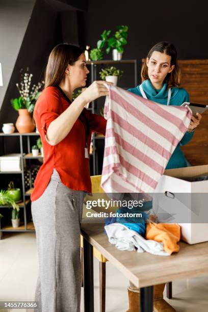 two young women folding and sorting clothes for donation and charity - clothing donation stock pictures, royalty-free photos & images