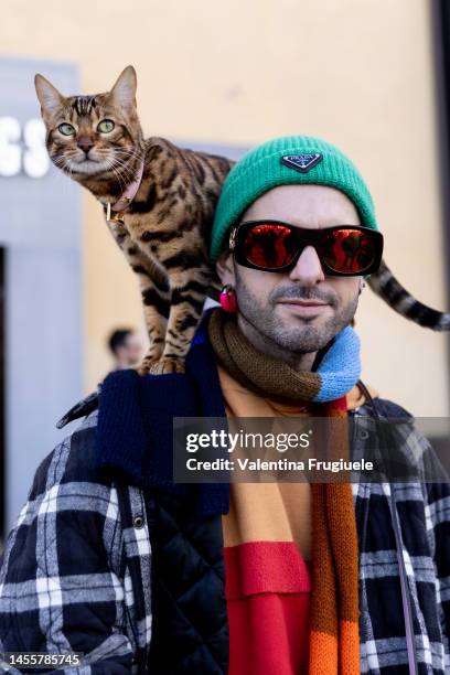 Guest wearing a checkered puffed coat, multicolor scarf, pink pants, ribbed green beanie and a bengala cat on a leash at Fortezza Da Basso on January...