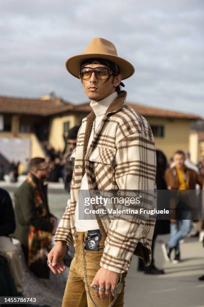 Guest wearing camel suede Diesel pants, a white turtleneck, checkered cargo jacket and fedora hat at Fortezza Da Basso on January 11, 2023 in...