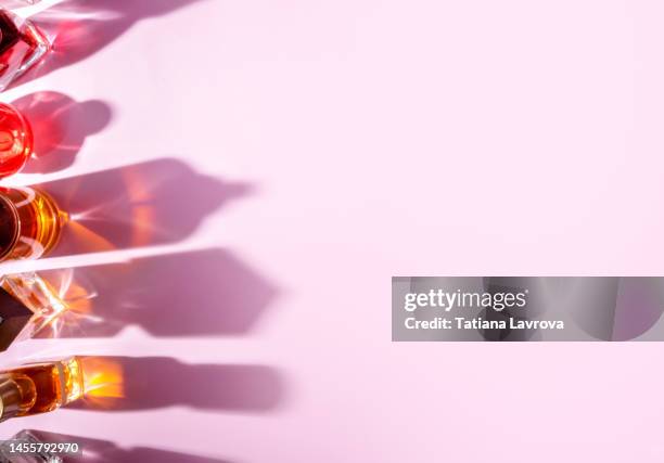 set of perfume bottles casting illuminating shadows on pink background. abstract beauty cosmetics photo with copy space. - perfumería fotografías e imágenes de stock