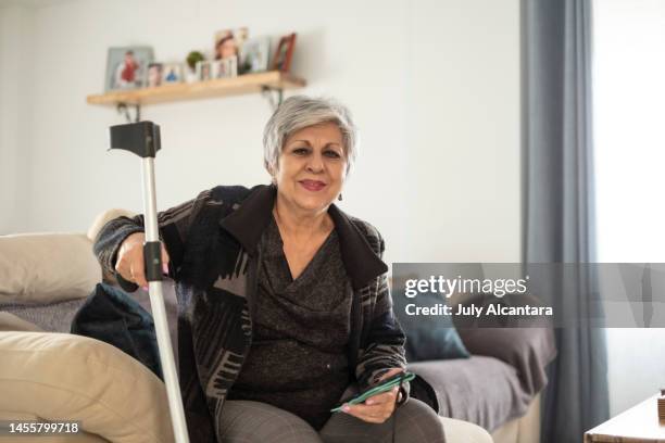 senior woman lifestyles at home on crutches due to rheumatic disease, smiling at camera - crutch stock pictures, royalty-free photos & images