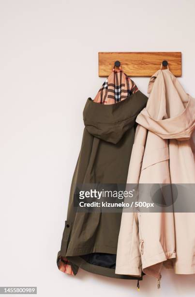 two jackets in beige and olive hang on a wooden wall hanger - coat hanging stock pictures, royalty-free photos & images