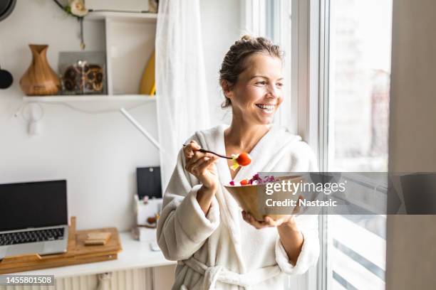 belle femme mangeant une salade de légumes saine portant un peignoir - équilibre alimentaire photos et images de collection