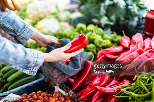 young adult woman buying red bell pepper at market with reusable bag - red pepper stock pictures, royalty-free photos & images