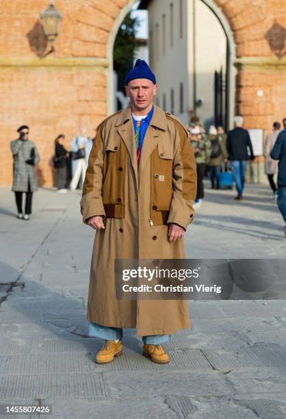 Matteo Marucci wears beige oversized coat, blue beanie, denim jeans, beige laced shoes at Fortezza Da Basso on January 11, 2023 in Florence, Italy.