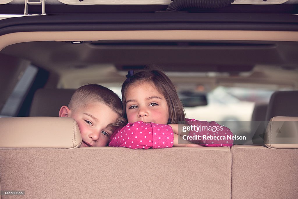 Brother and sister look out back of their car