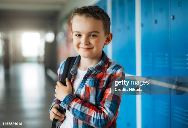 elementary schoolboy standing in front of lockers in school corridor - school boy with bag stock pictures, royalty-free photos & images