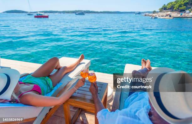 couple relaxing and toasting with a spritz cocktail on a beach deck over the ocean - kroatien strand stock pictures, royalty-free photos & images