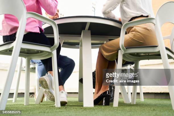 low angle of coworkers gathered together sharing or talking, sitting at a rooftop table with a rear view of two women - businesswoman under stock-fotos und bilder