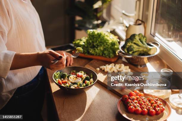 healthy dinner or lunch. woman in t-shirt and jeans standing and holding vegan superbowl or buddha bowl with hummus, vegetable, salad, beans, couscous and avocado and smoothie in hands, square crop - kreuzblütengewächse stock-fotos und bilder
