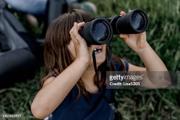 cute female child looks through binoculars outdoors in nature having an adventure - children binocular stockfoto's en -beelden