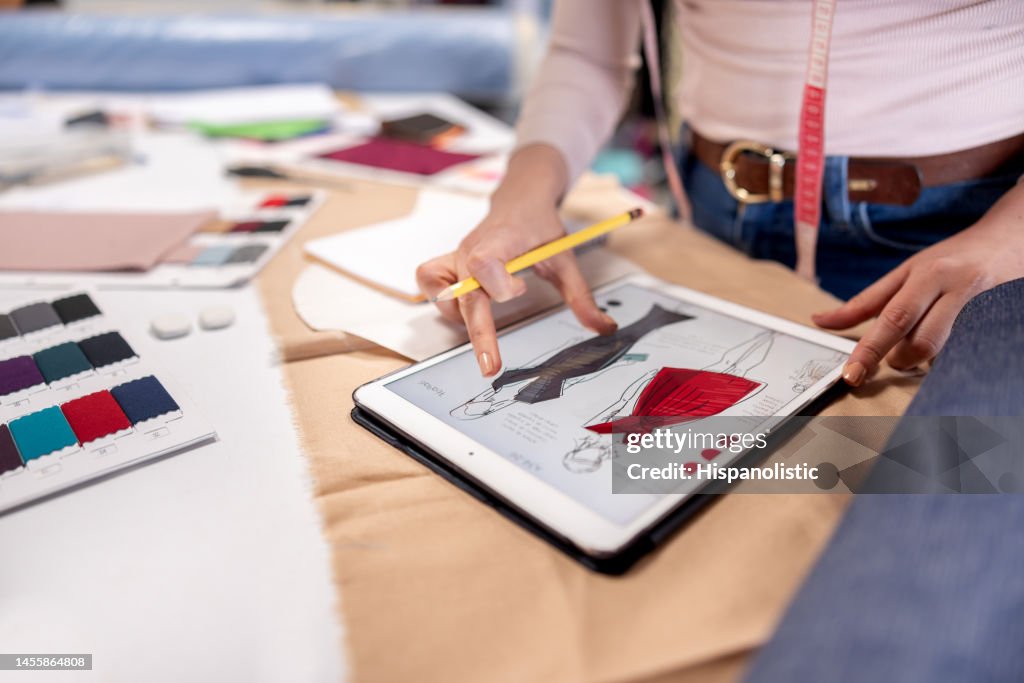 Diseñadora de moda dibujando vestidos en su taller usando una tableta
