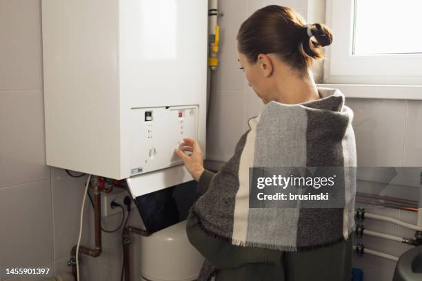 a woman reduces the power of the gas boiler in her home due to an energy crisis - gas boiler stock pictures, royalty-free photos & images